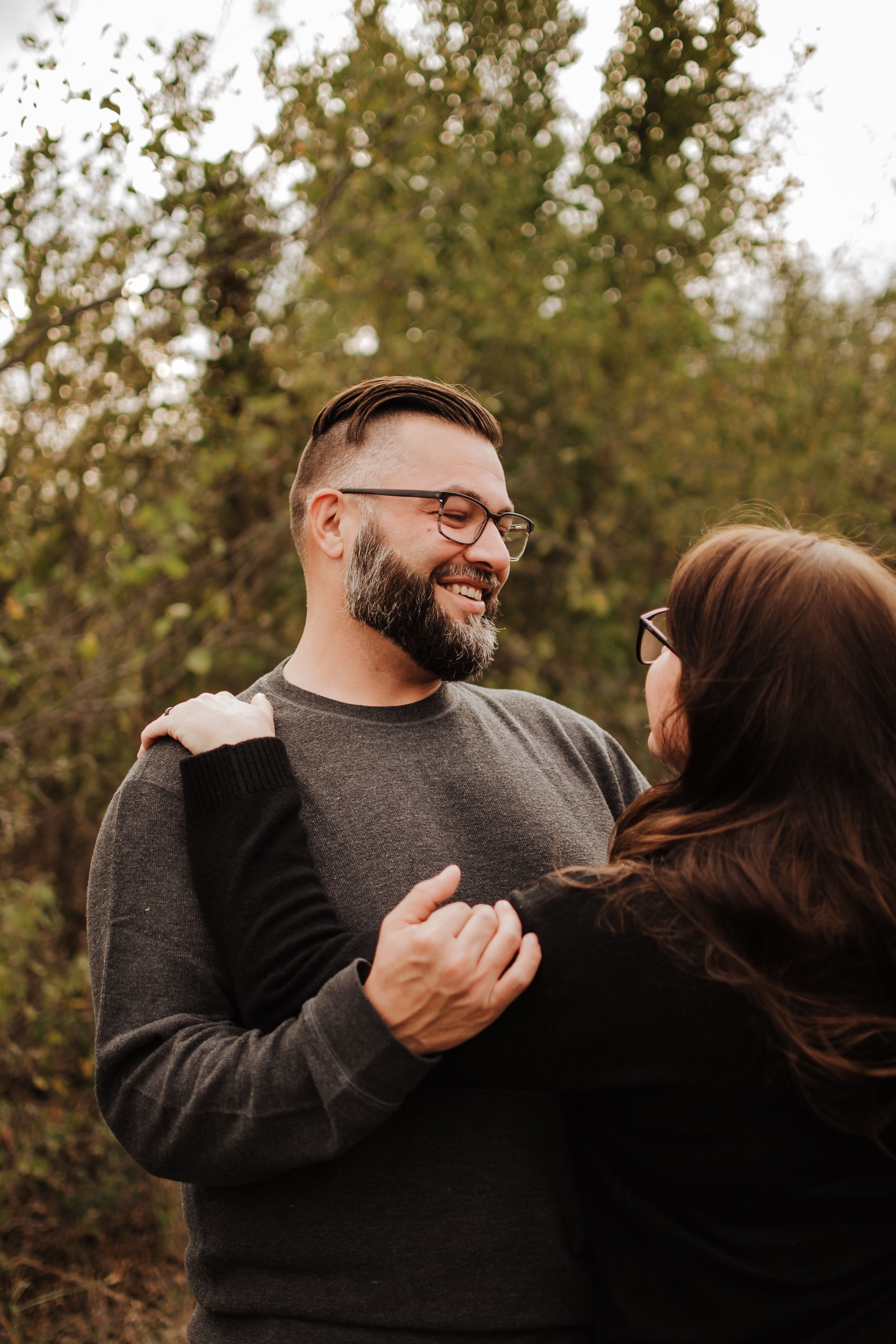 A couple shares a tender moment of laughter together against a backdrop of fall foliage.