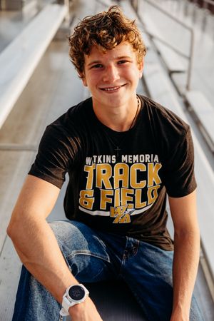 Track athlete seated in stadium wearing black Vikings Memorial Track and Field t-shirt.