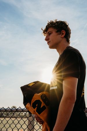 A series of silhouettes shows someone leaning against a chain link fence at sunset with a golden sun glow behind them.