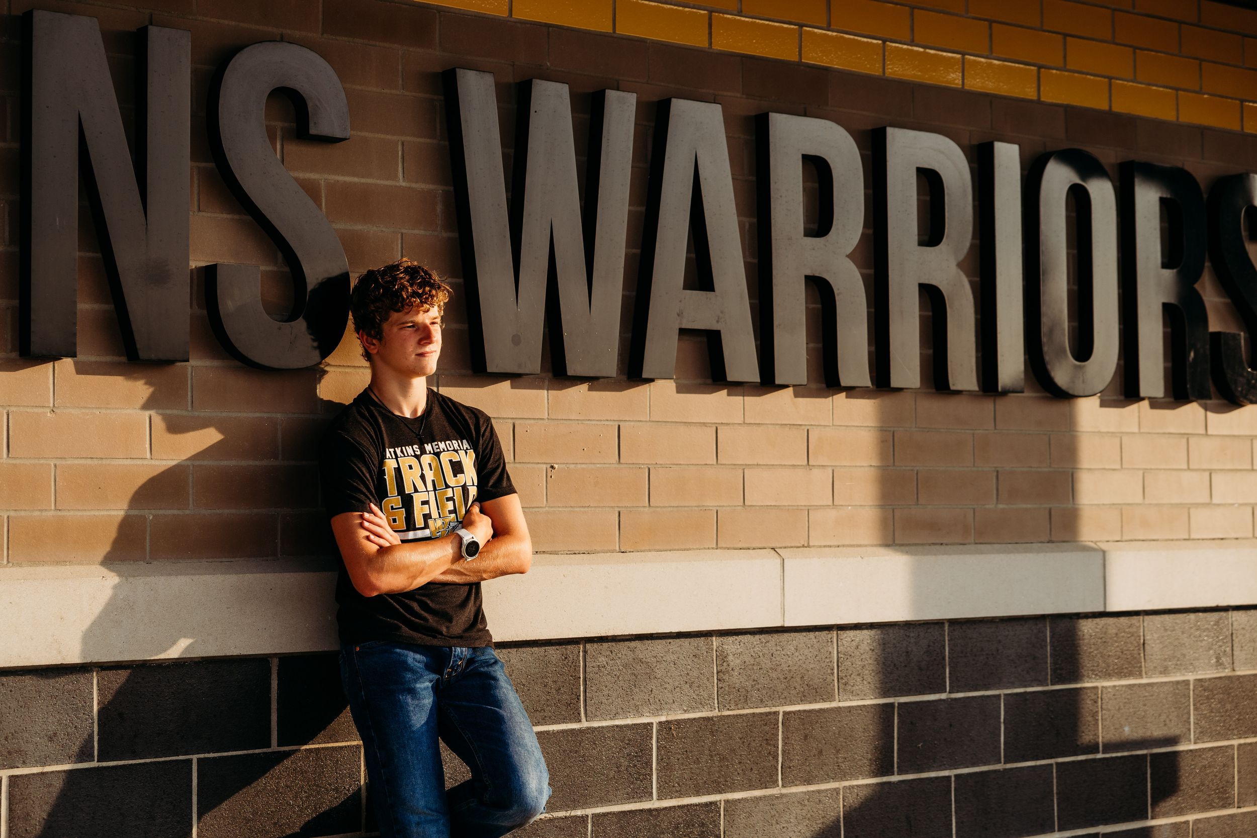 A lone person in a black t-shirt leans against a brick wall with dramatic side lighting and text visible above.
