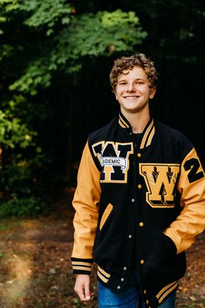 High school letterman jacket senior portrait photos taken outdoors showing black and gold varsity jacket in wooded setting.