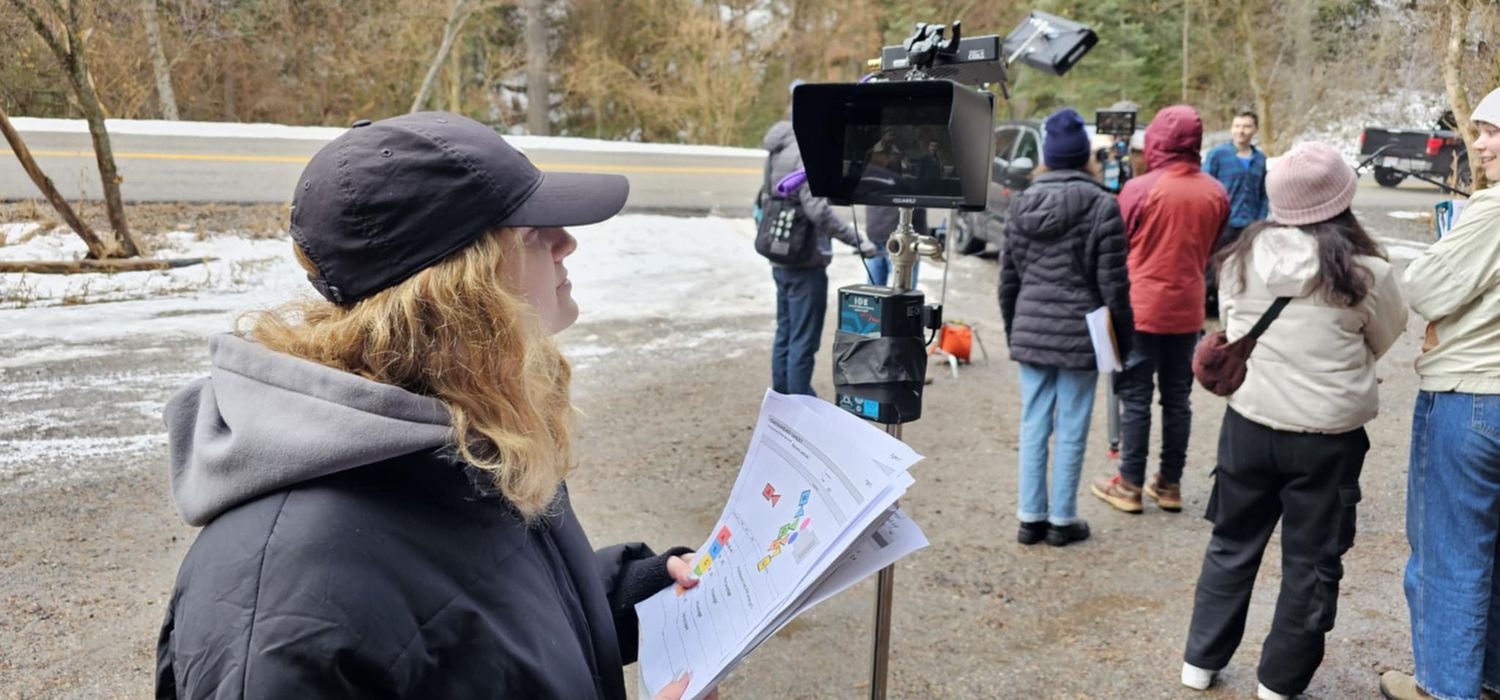 A film crew reviews storyboards outdoors in winter, with a camera operator and director on location.