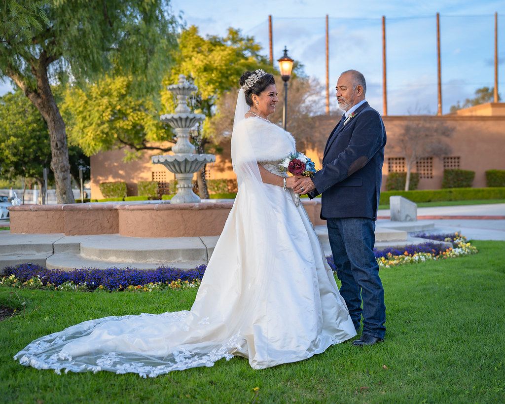 Bride and groom hold hands on a lawn in front of a fountain at sunset.