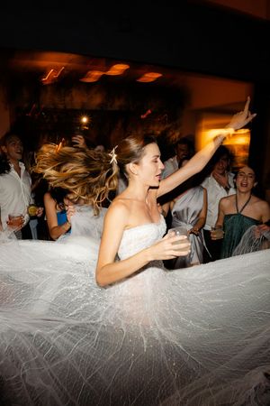 Wedding party guests celebrate on dance floor under a flowing white tulle fabric at a reception.