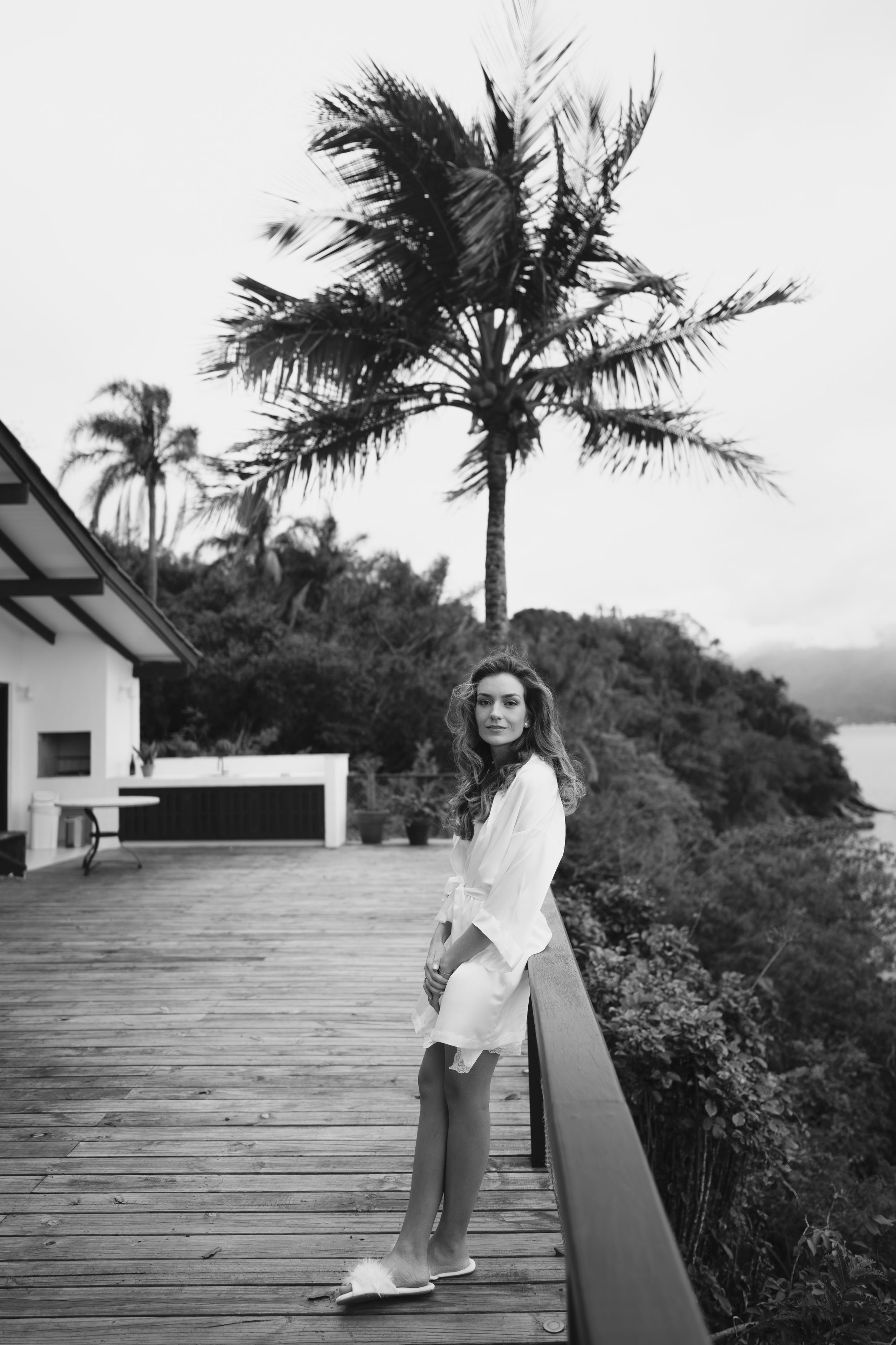 Black and white photo series of a person sitting on a seaside deck with palm trees and ocean view in the background.
