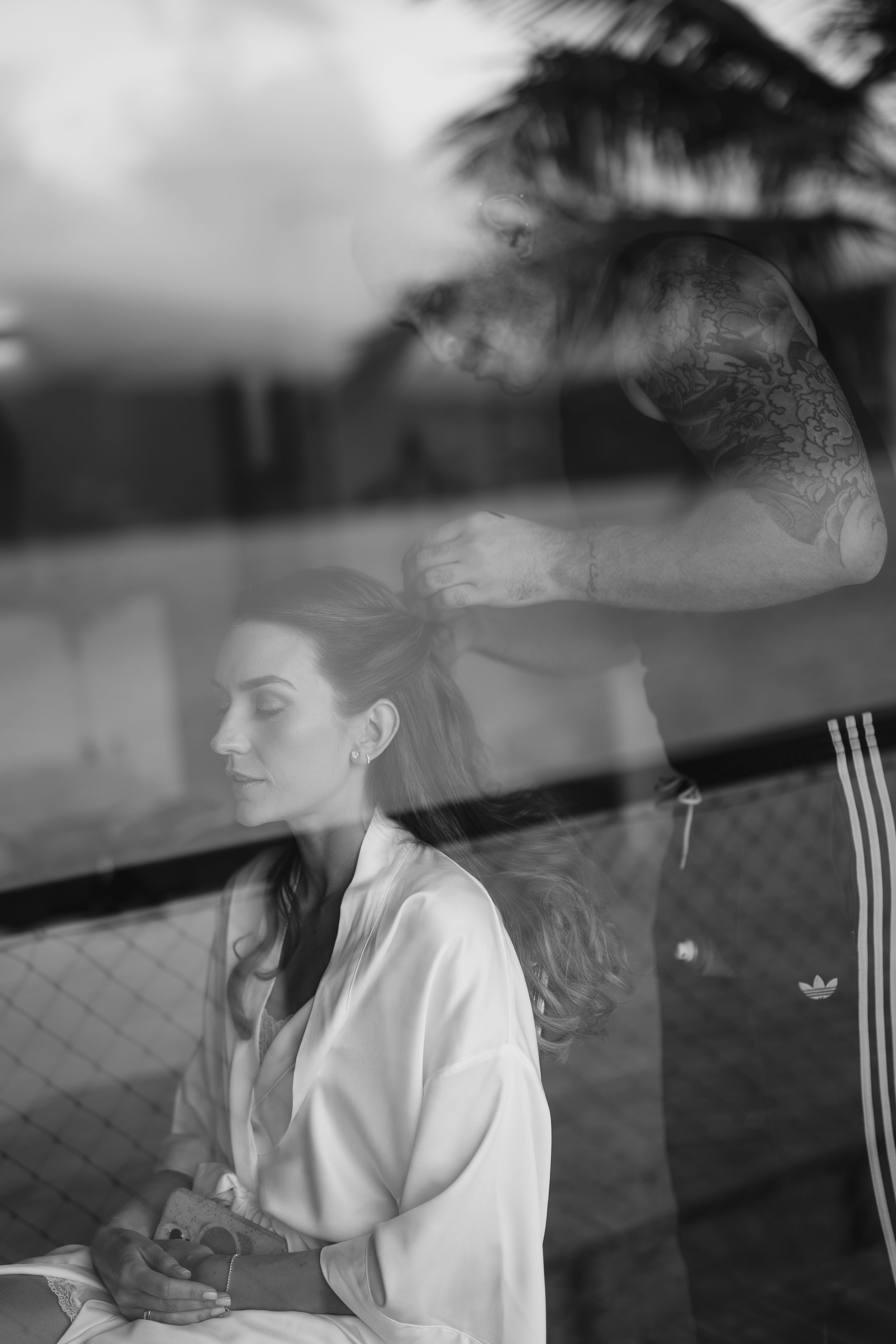 A moody black and white artistic double exposure portrait through glass showing reflection and contemplative pose.