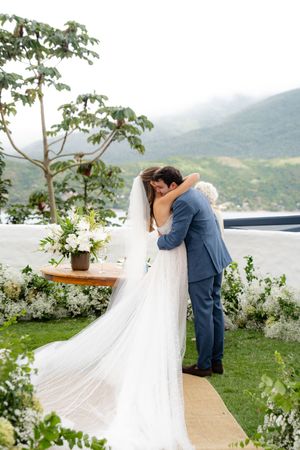 A couple shares an intimate moment at their lakeside wedding ceremony with mountain views and white floral decor.