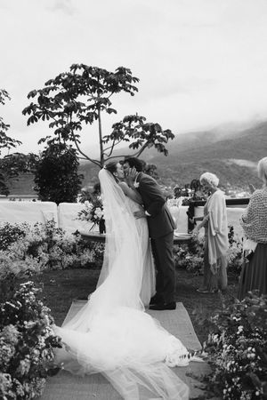 A romantic outdoor wedding ceremony takes place in a mountain garden setting with a flowing white wedding dress.