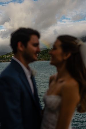 A romantic wedding couple shares multiple kisses by the ocean with dramatic cloudy skies and coastline in the background.
