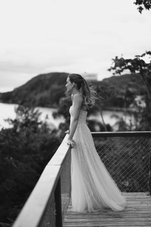 A sequence of black and white photos showing a bride in a flowing wedding dress standing on a wooden deck at sunset.