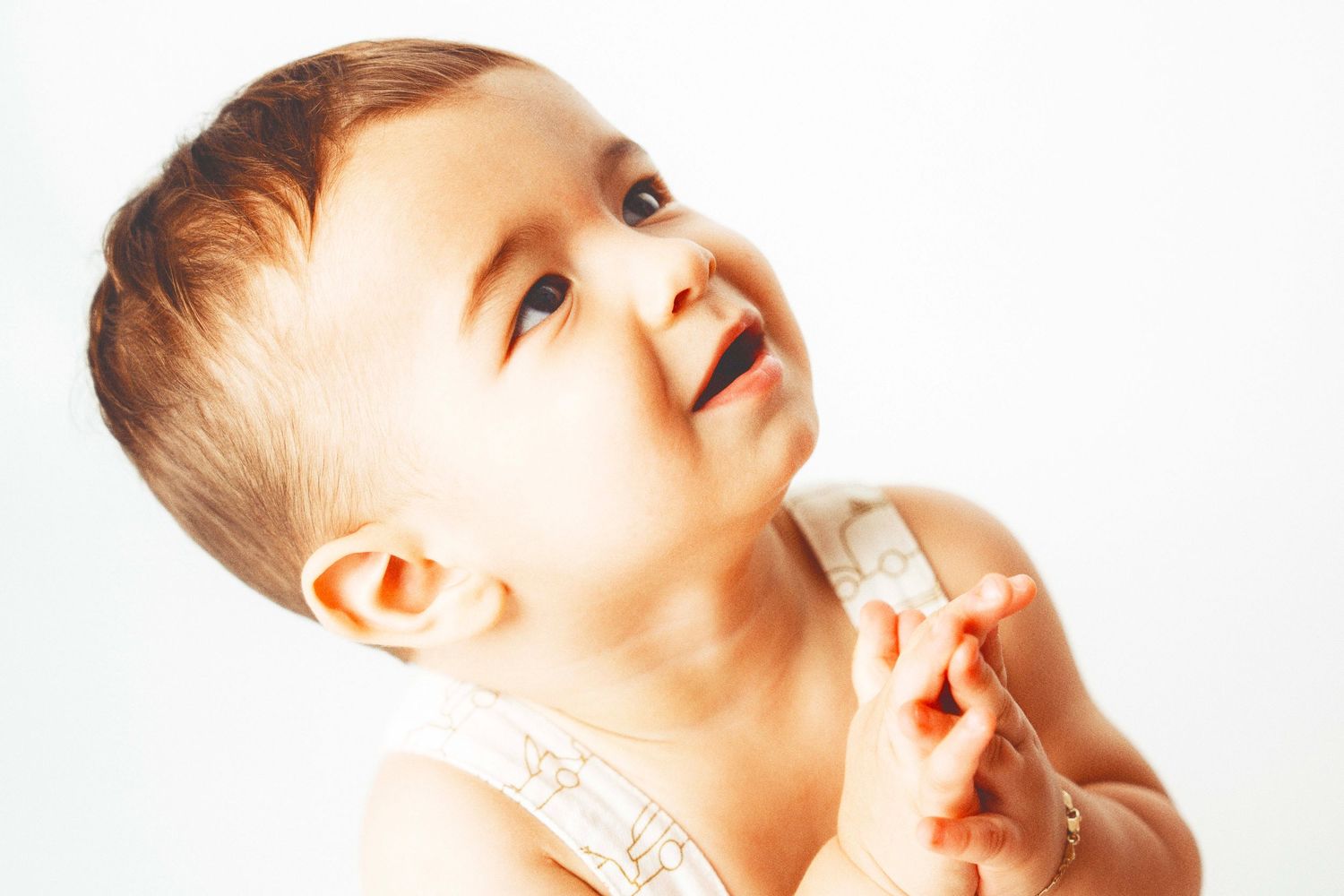 Small child looking upward with a smile while being held by someone out of frame against white background.