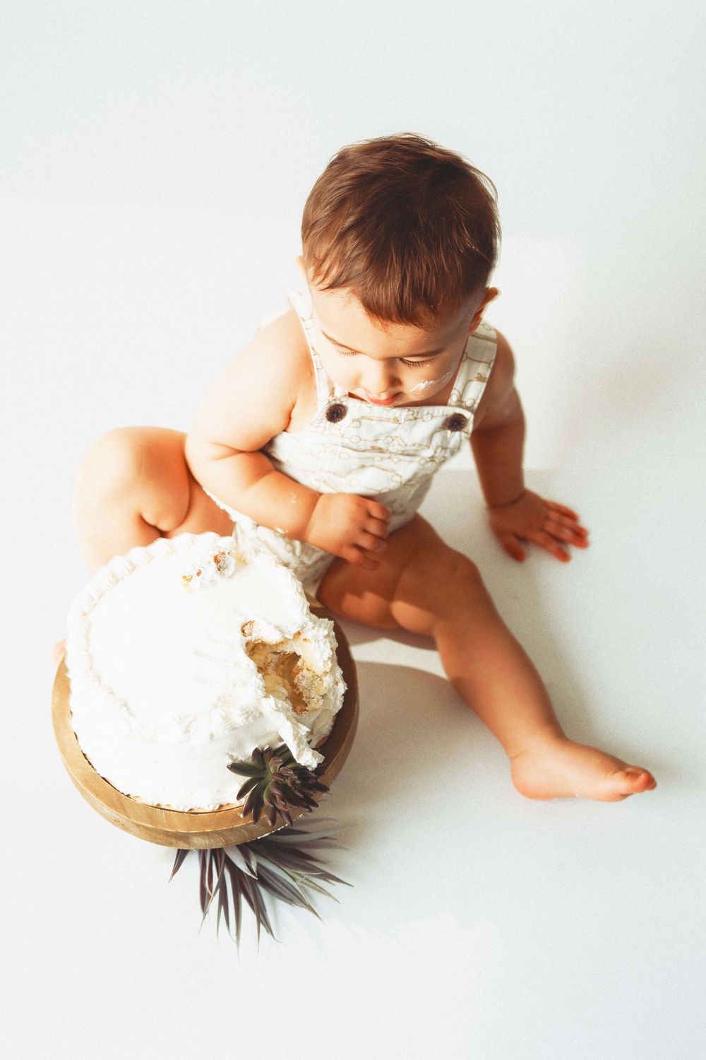 Baby in white overalls playing with a decorated coconut on white background.