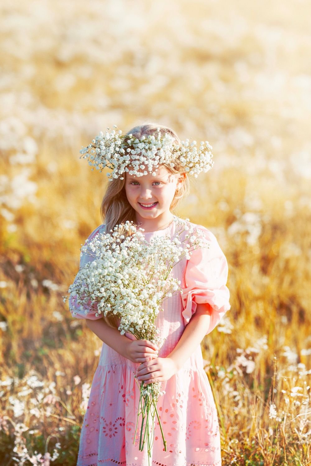 Sun-drenched portrait with baby's breath flower crown and bouquet in pink dress.