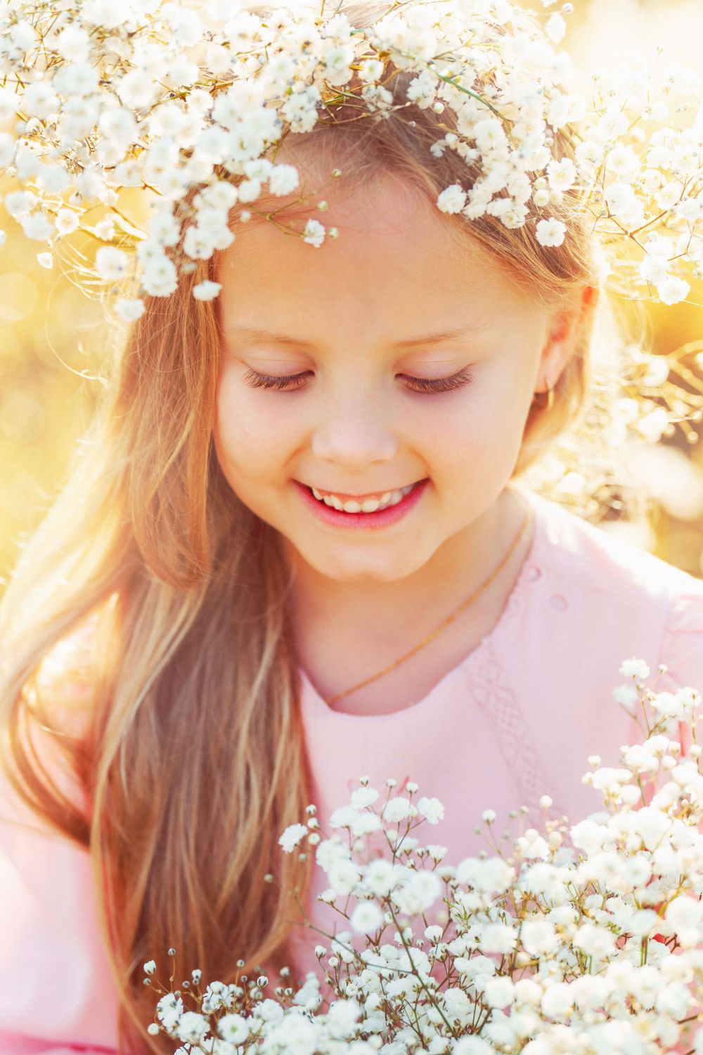 Portrait in pink dress with baby's breath flower crown amid golden sunlit field.