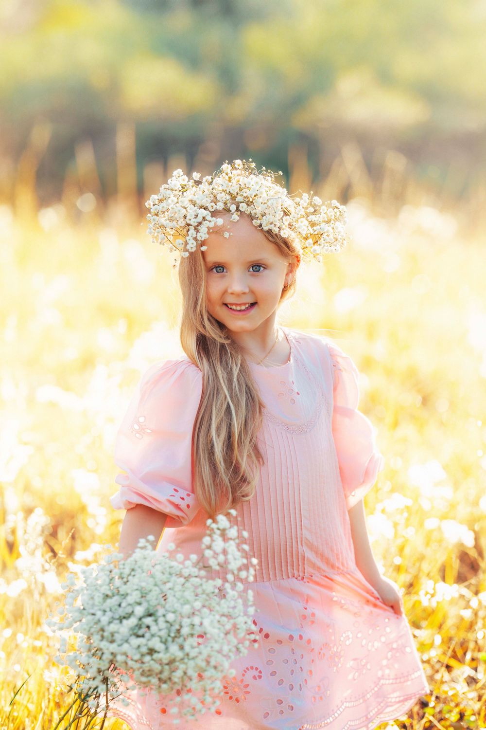 Dreamy outdoor portrait with floral crown and baby's breath bouquet in golden field.