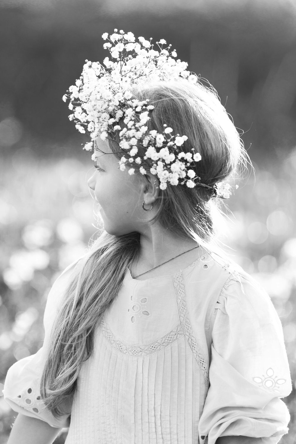 Black and white portrait with baby's breath flower crown in sunlit field.