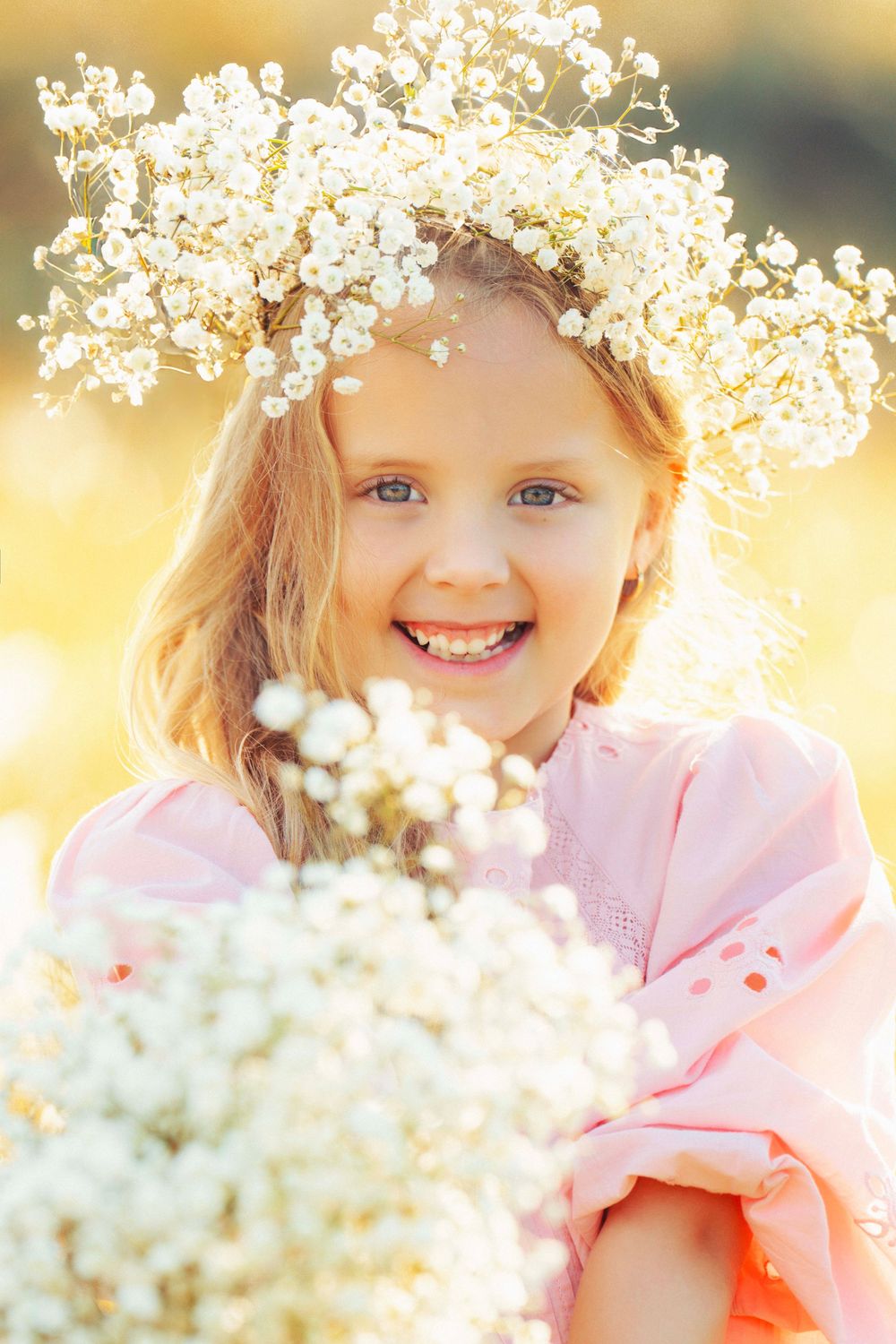 Close up portrait wearing baby's breath crown and pink dress in golden sunlight.