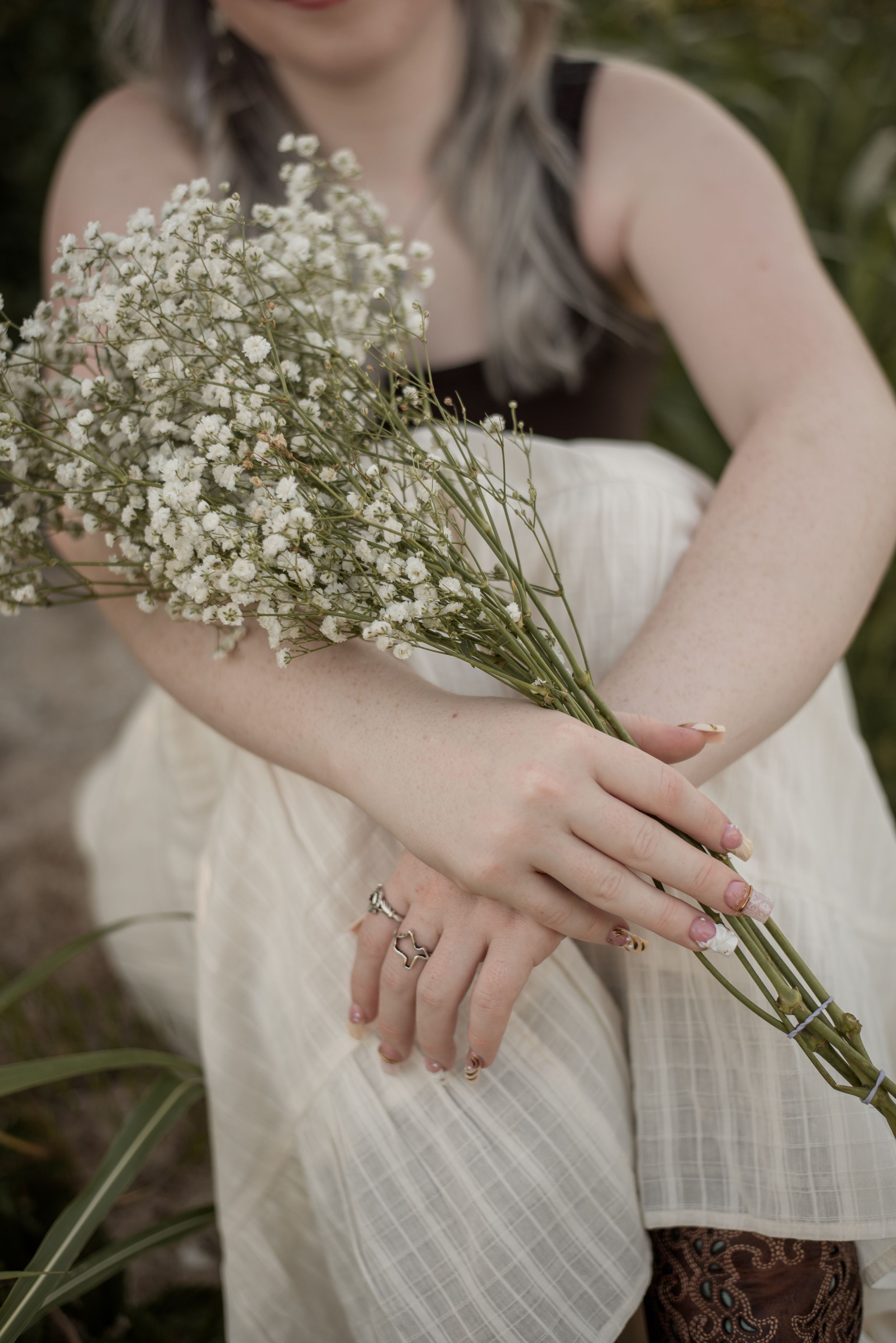 Close-up of a woman in a white linen dress holding a delicate bouquet of white baby's breath flowers.
