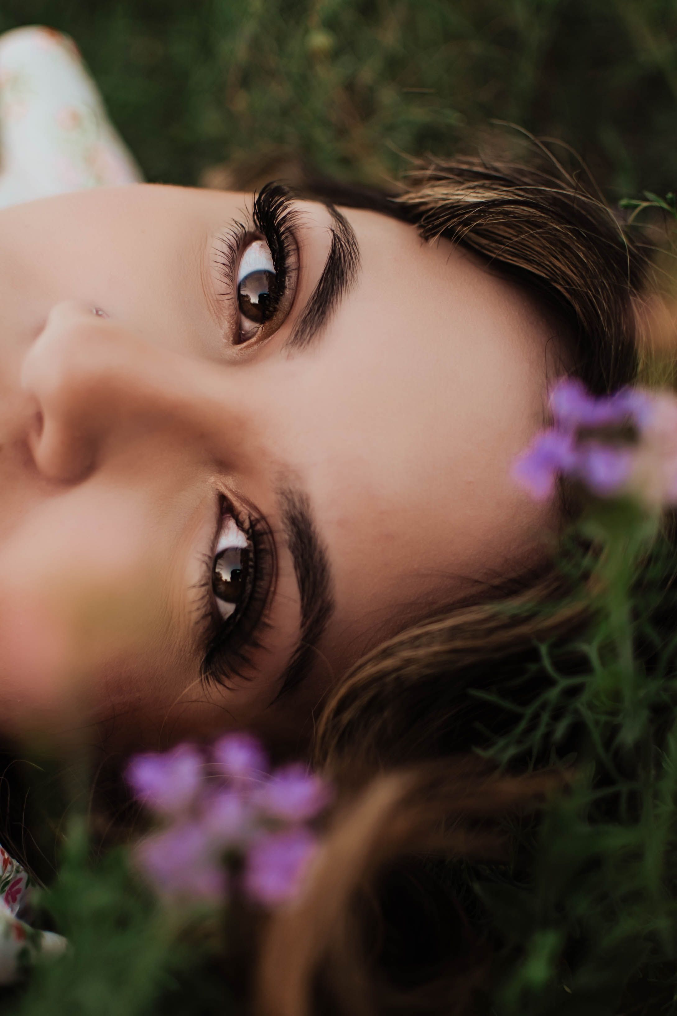 A close-up artistic photograph showing dramatic eyes and eyelashes among purple wildflowers. Tandy Hills