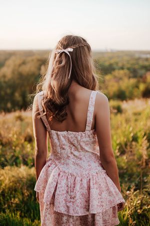 A person in a floral sundress standing against a sunset backdrop in a meadow. Tandy Hills