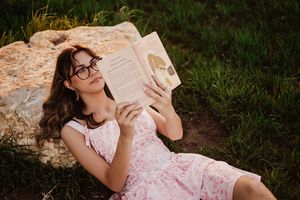 Someone reading a book while relaxing against a large rock in a pink floral dress. Tandy Hills