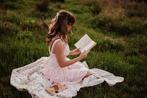A peaceful scene of reading outdoors in a pink dress on a white blanket. Tandy Hills