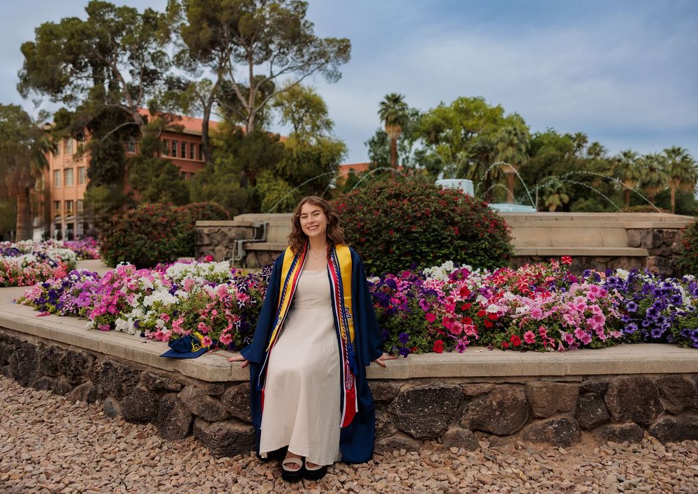 University of Arizona grad with cap and gown on campus – UArizona graduation pictures at Old Main with flowers