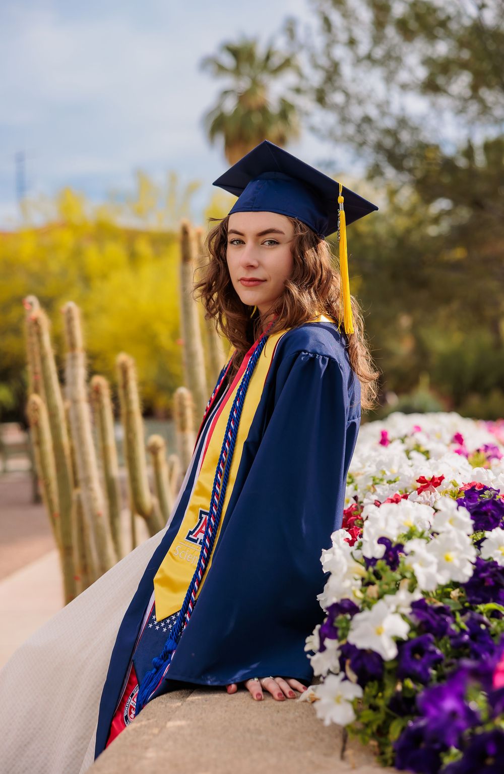 University of Arizona grad with cap and gown on campus – UArizona graduation pictures at Old Main with flowers