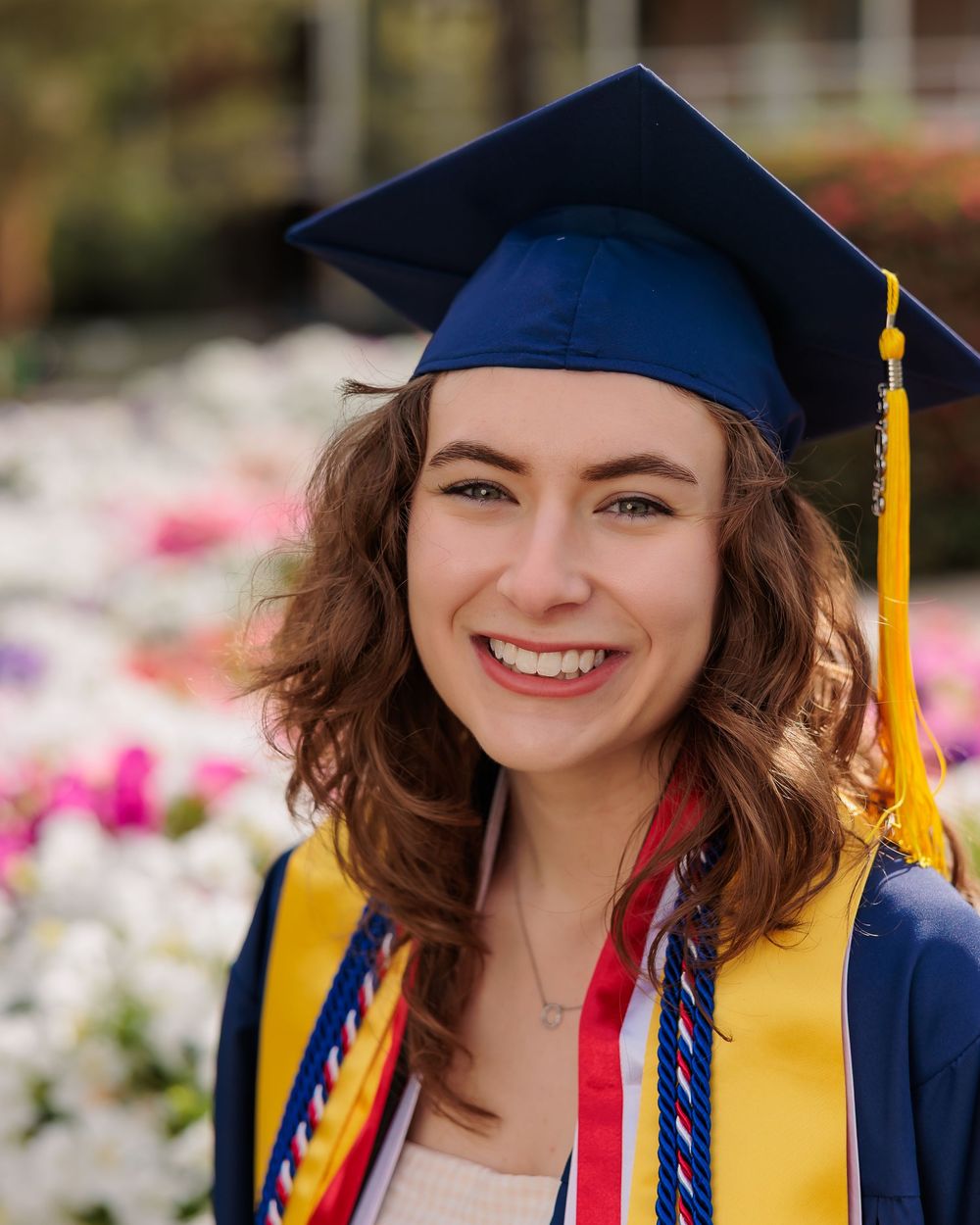 University of Arizona grad with cap and gown on campus – UArizona graduation pictures at Old Main with flowers