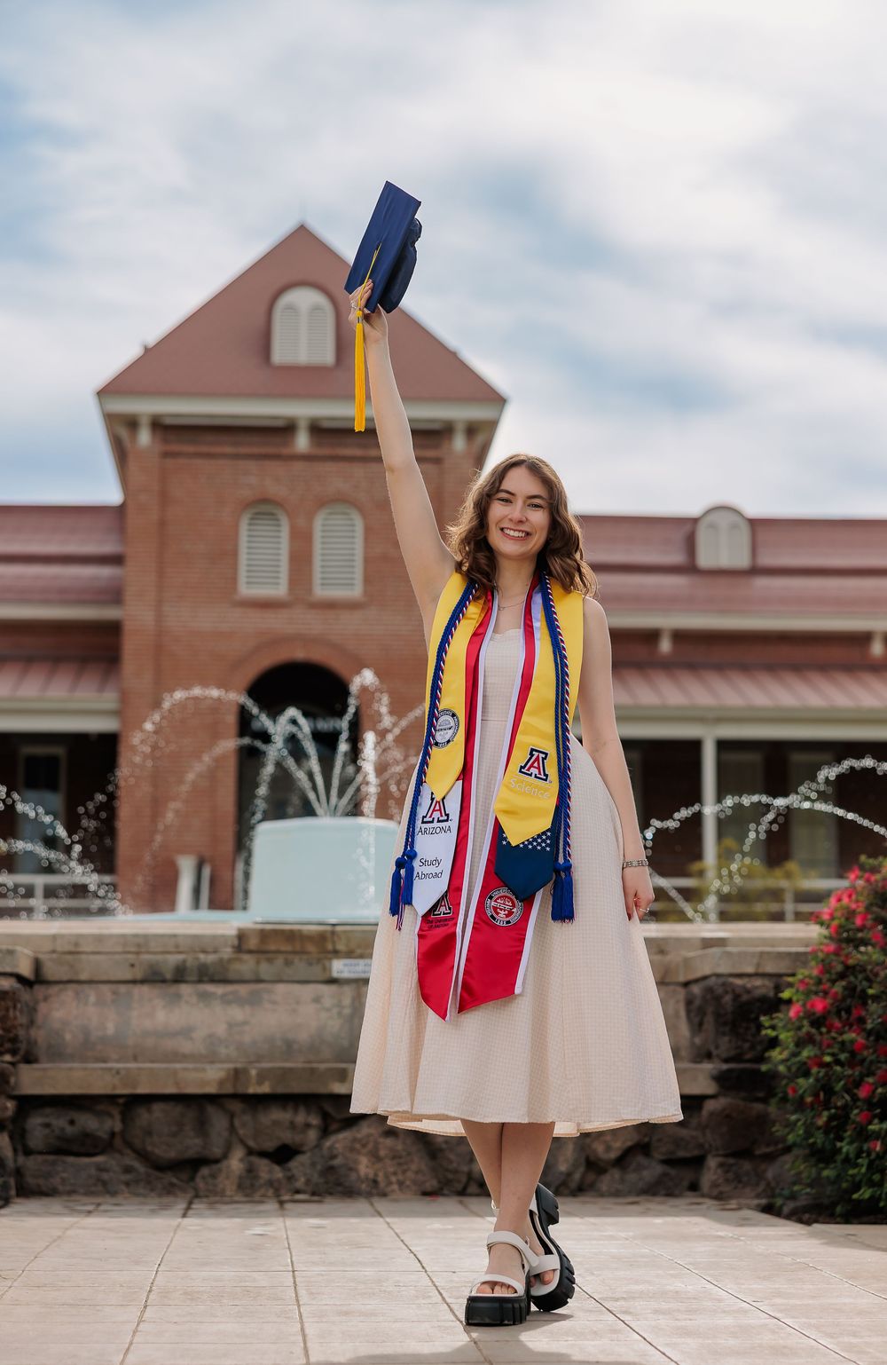 University of Arizona grad with cap and gown on campus – UArizona graduation pictures at Old Main with flowers