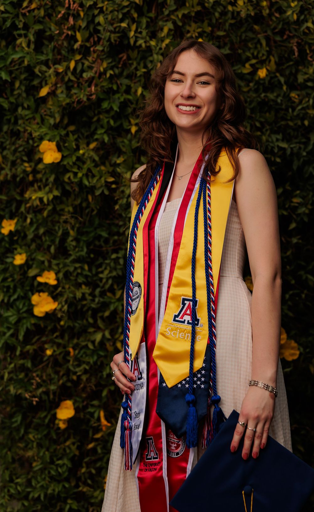 University of Arizona grad with cap and gown on campus – UArizona graduation pictures at Old Main with flowers