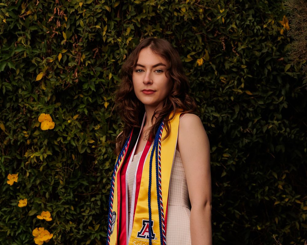 University of Arizona grad with cap and gown on campus – UArizona graduation pictures at Old Main with flowers