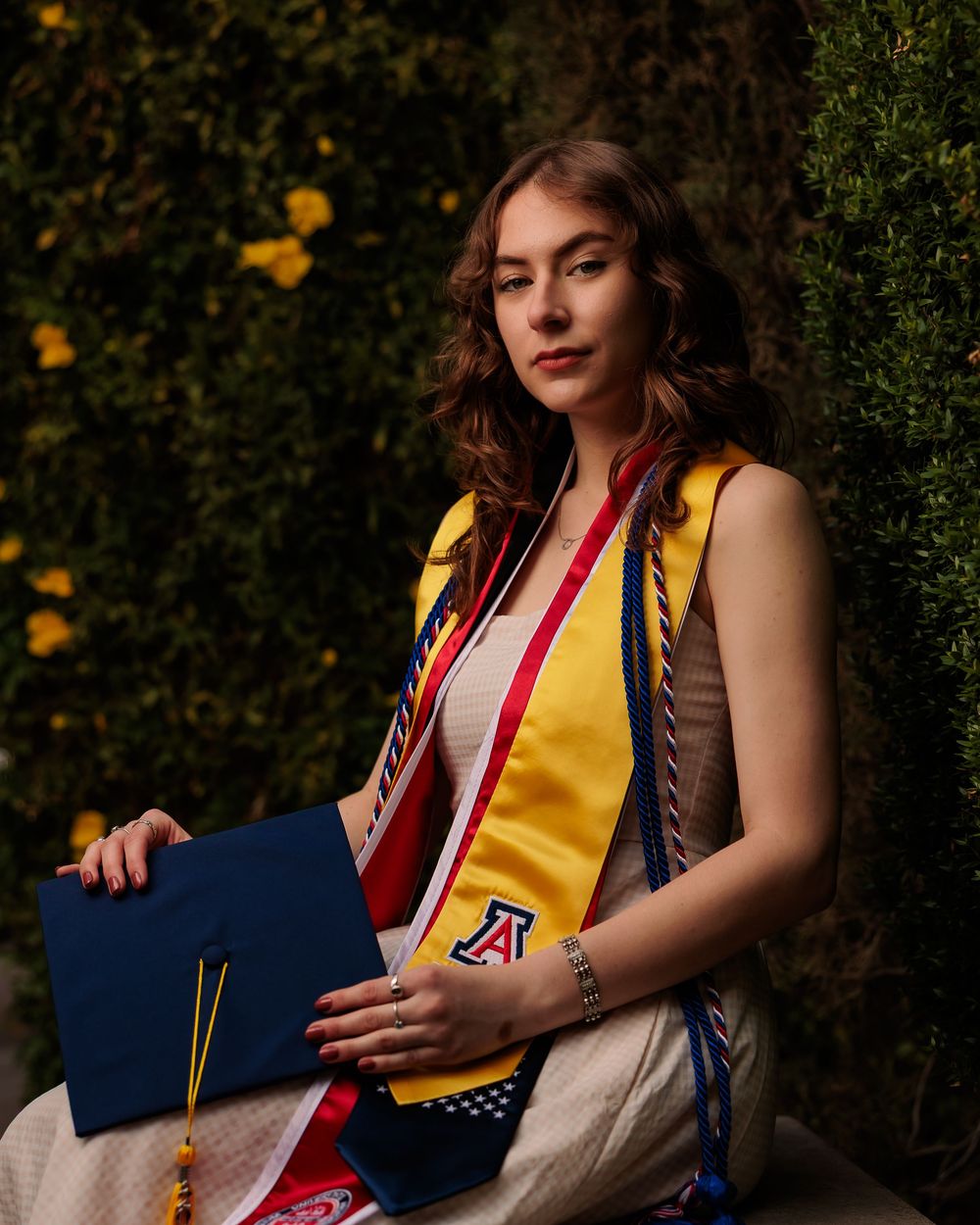University of Arizona grad with cap and gown on campus – UArizona graduation pictures at Old Main with flowers