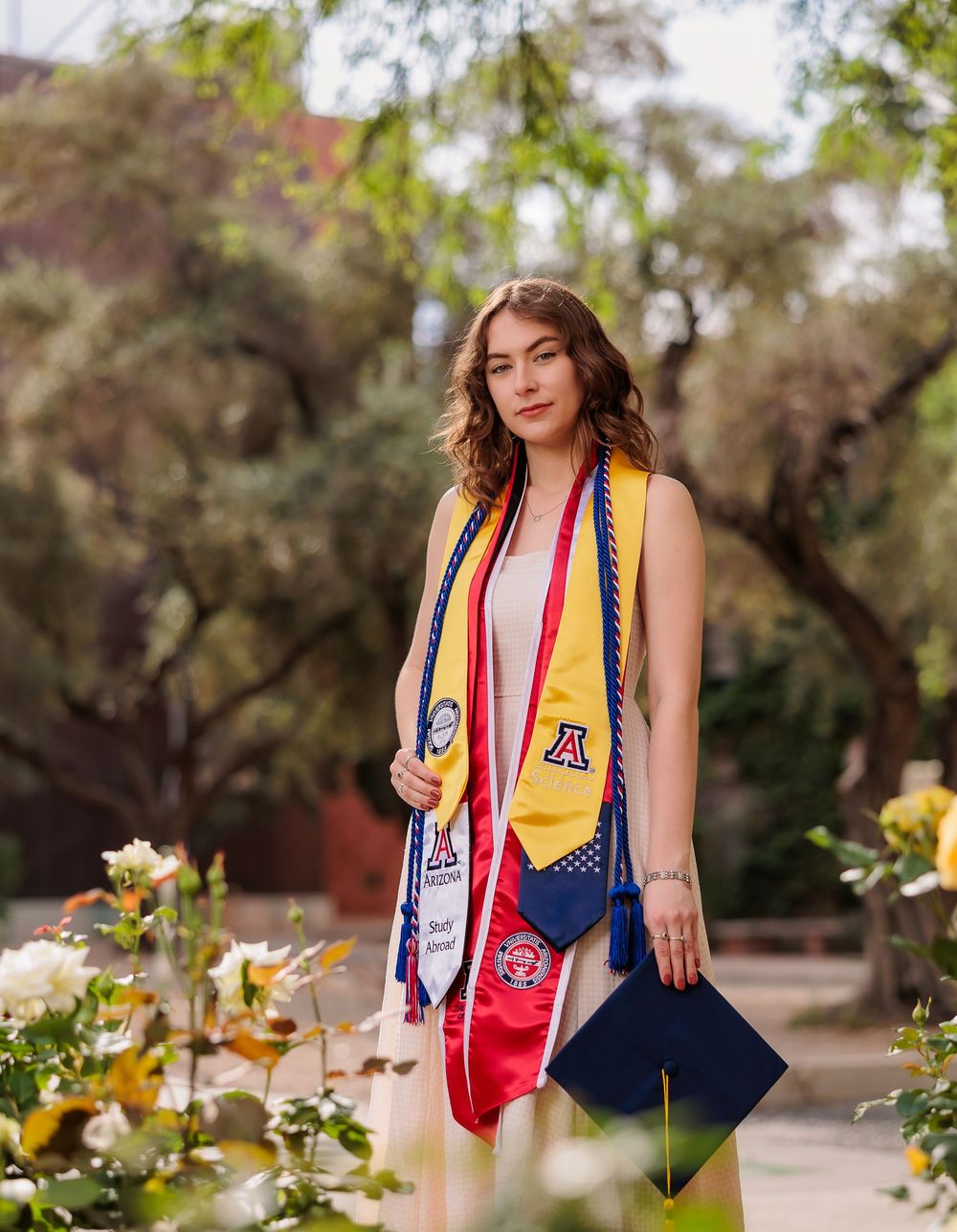 University of Arizona grad with cap and gown on campus – UArizona graduation pictures at Old Main with flowers
