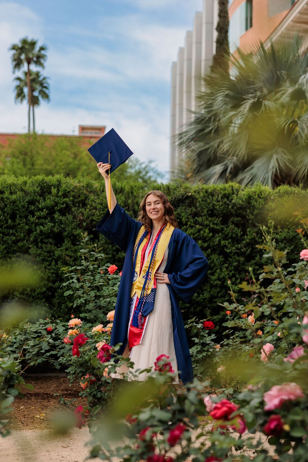 University of Arizona grad with cap and gown on campus – UArizona graduation pictures at Old Main with flowers