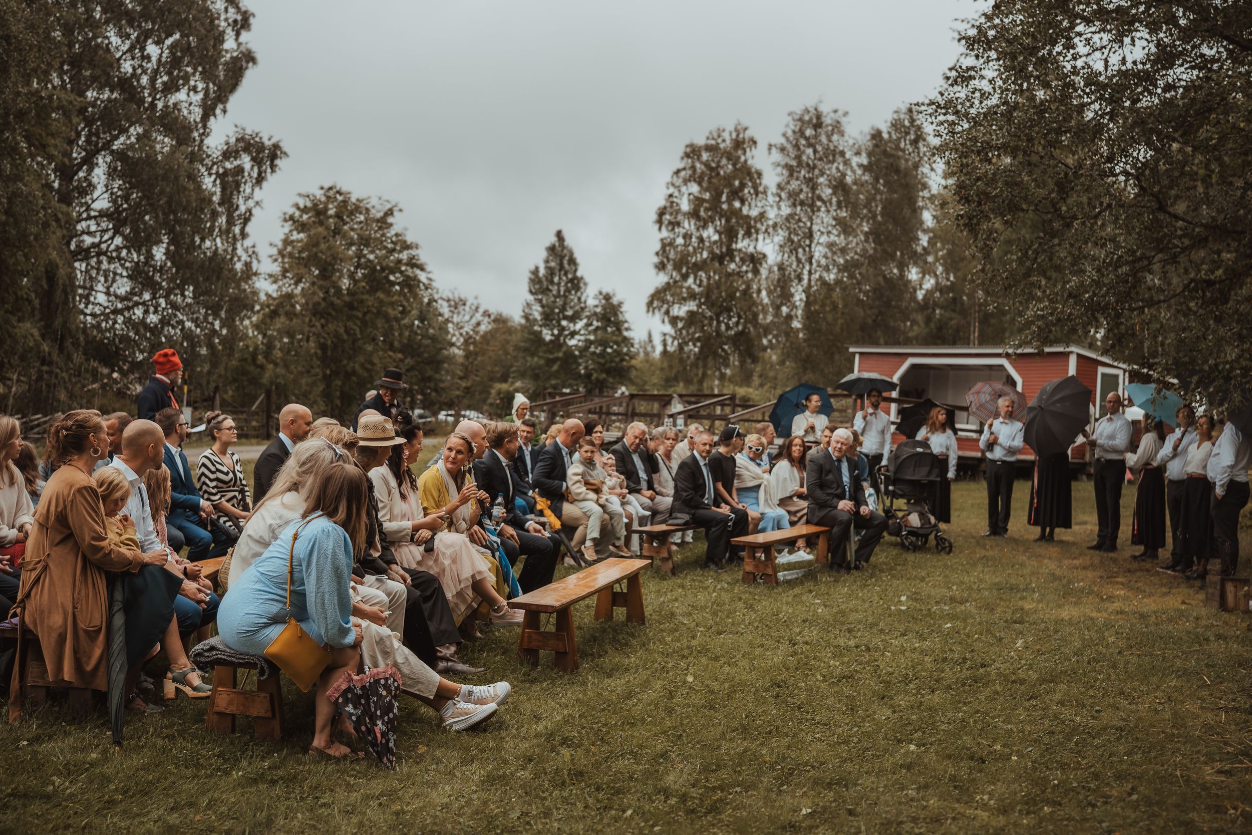 Guests gathered at an outdoor wedding celebration with food trucks and wooden benches on a cloudy autumn day.
