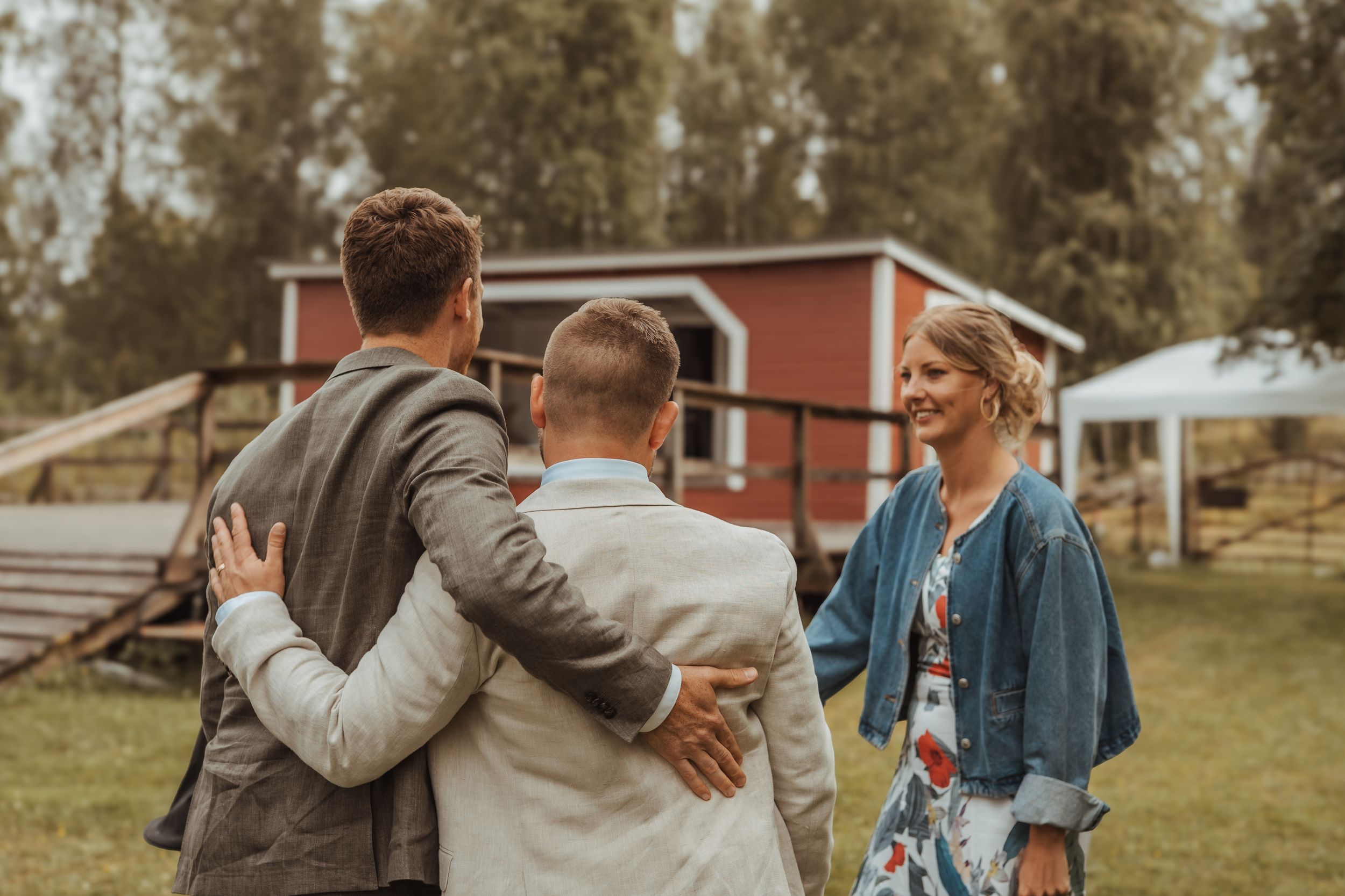 A casual couple embraces while walking together outdoors on a sunny autumn day with rustic buildings in background.