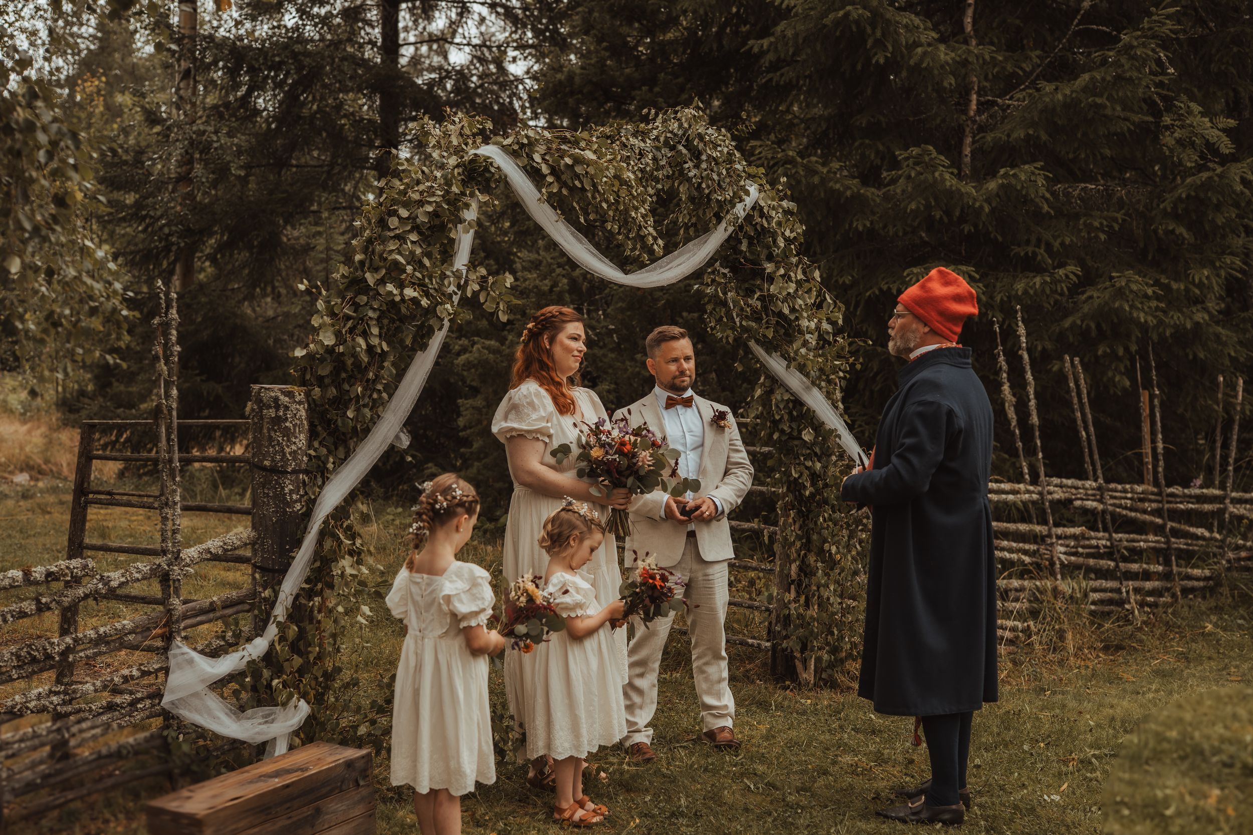 Wedding ceremony at twilight under a rustic wooden arch in a serene forest setting with loved ones gathered around.