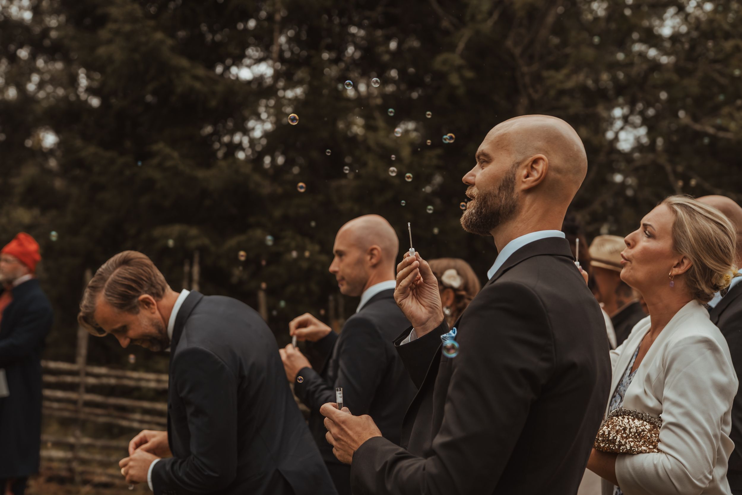 Candid moment of guests reacting with joy and taking photos during an outdoor wedding ceremony.