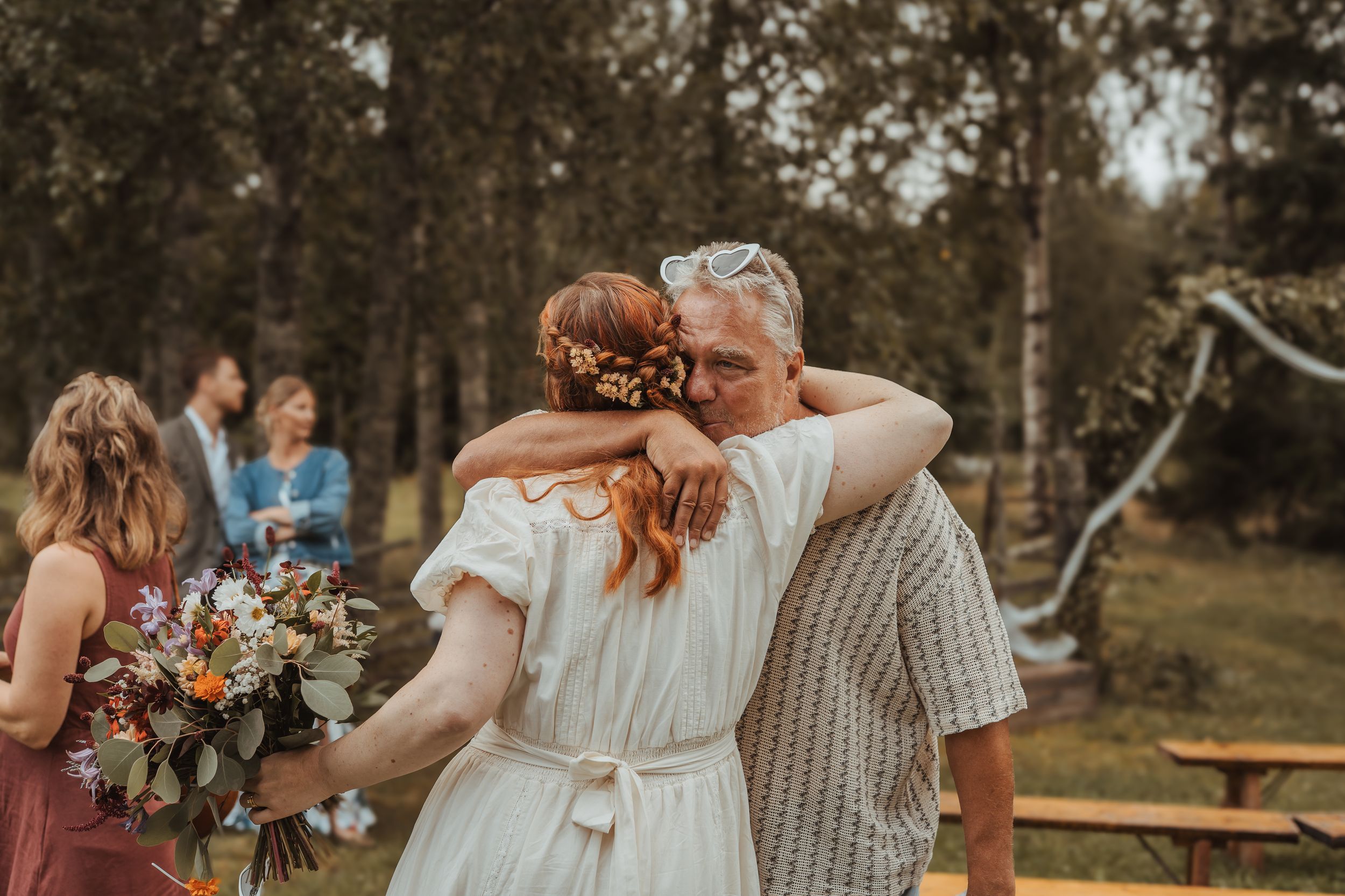 A couple embraces during an intimate outdoor wedding ceremony with floral bouquets and summer decor.