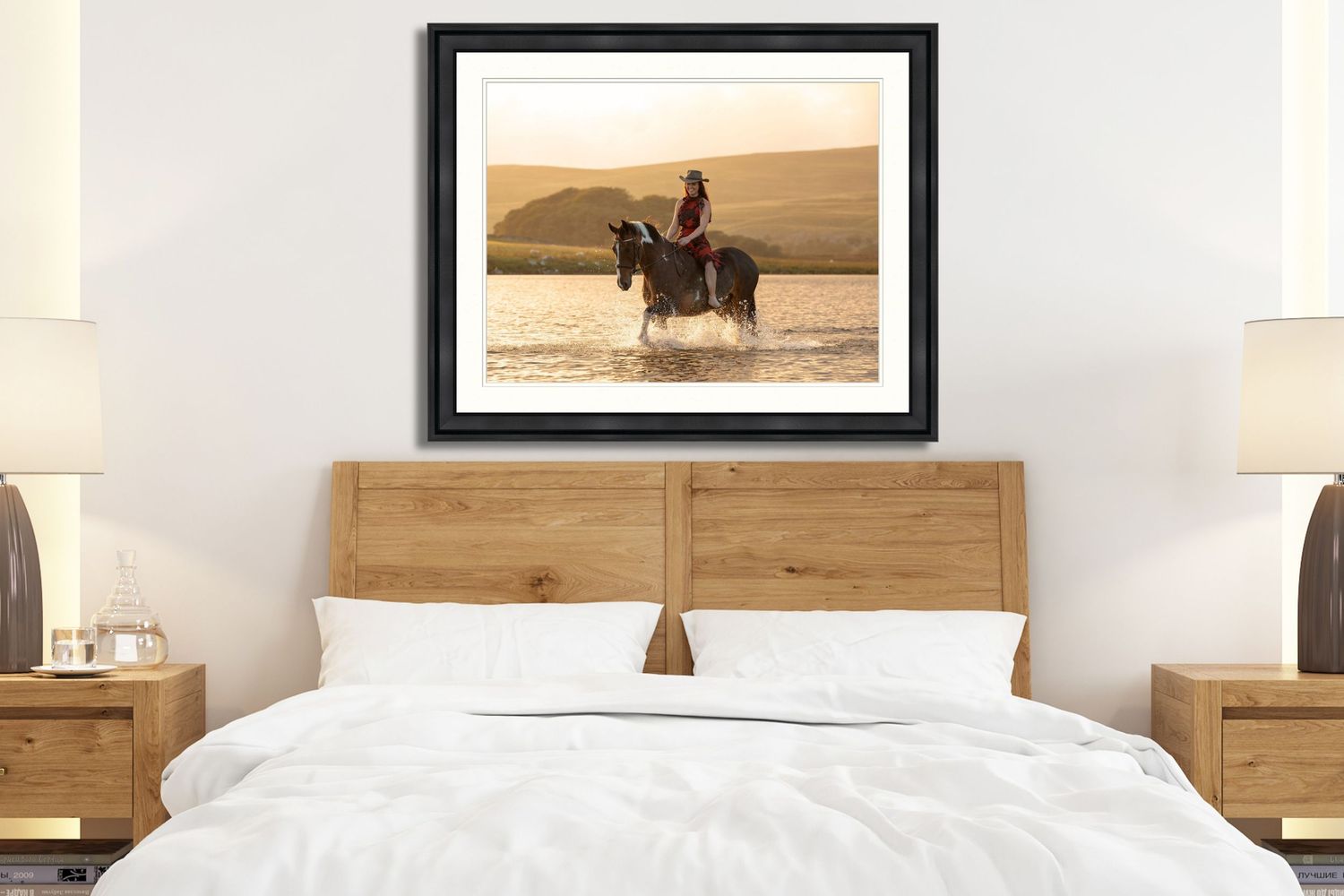 A framed photograph of a horse rider crossing a misty lake at sunset hangs above a modern wooden bed frame.
