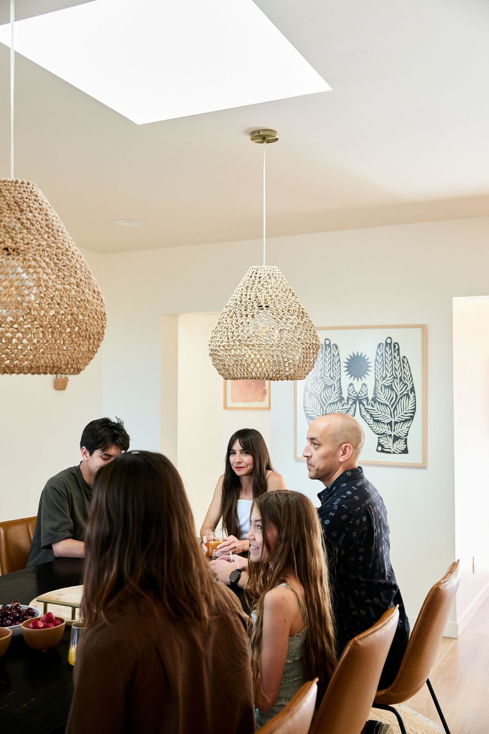 A group gathers under woven rattan pendant lights in a modern dining space with white walls and minimalist decor.