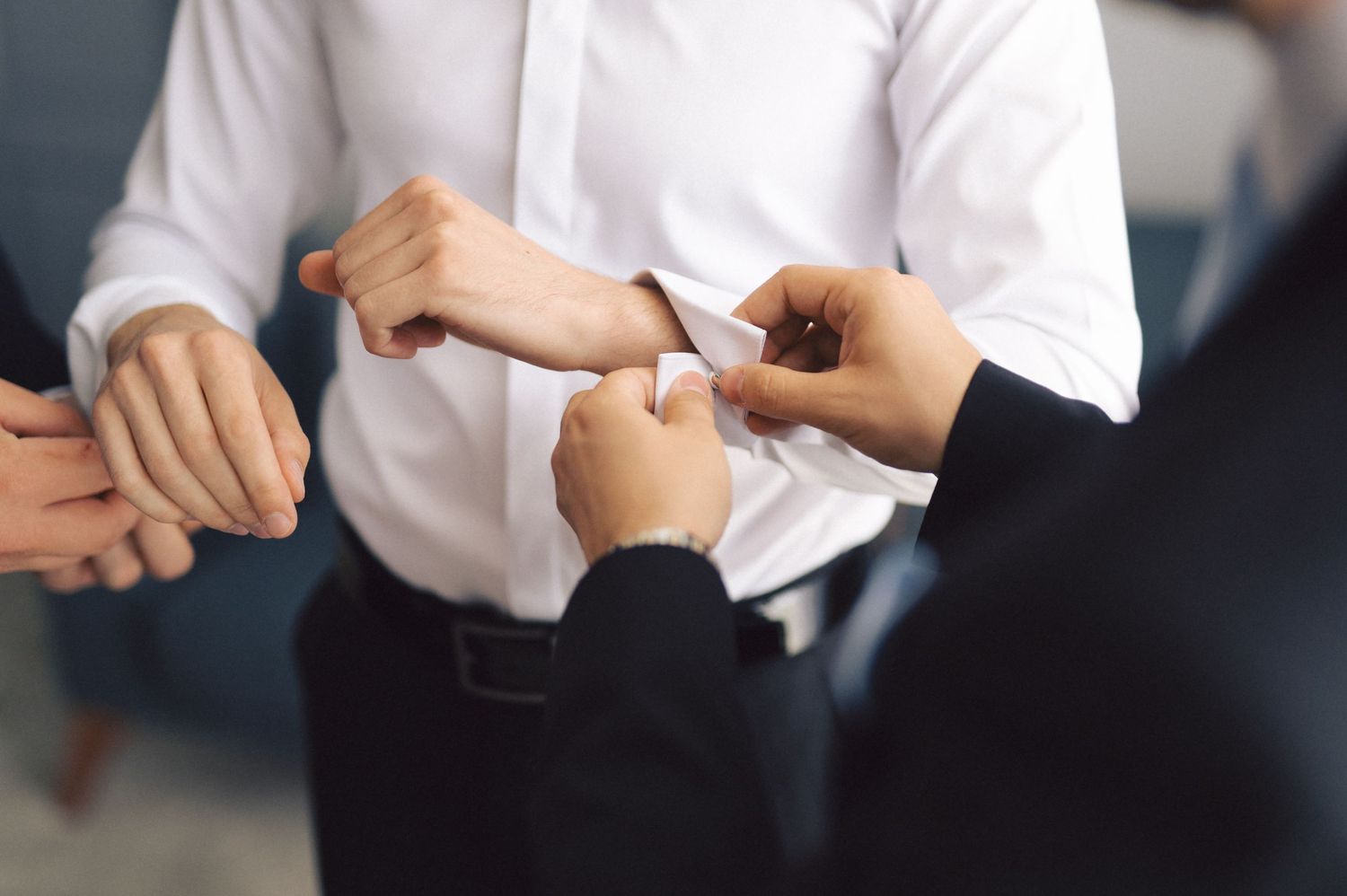 Hands adjusting white shirt buttons in a formal setting during preparation or dressing.