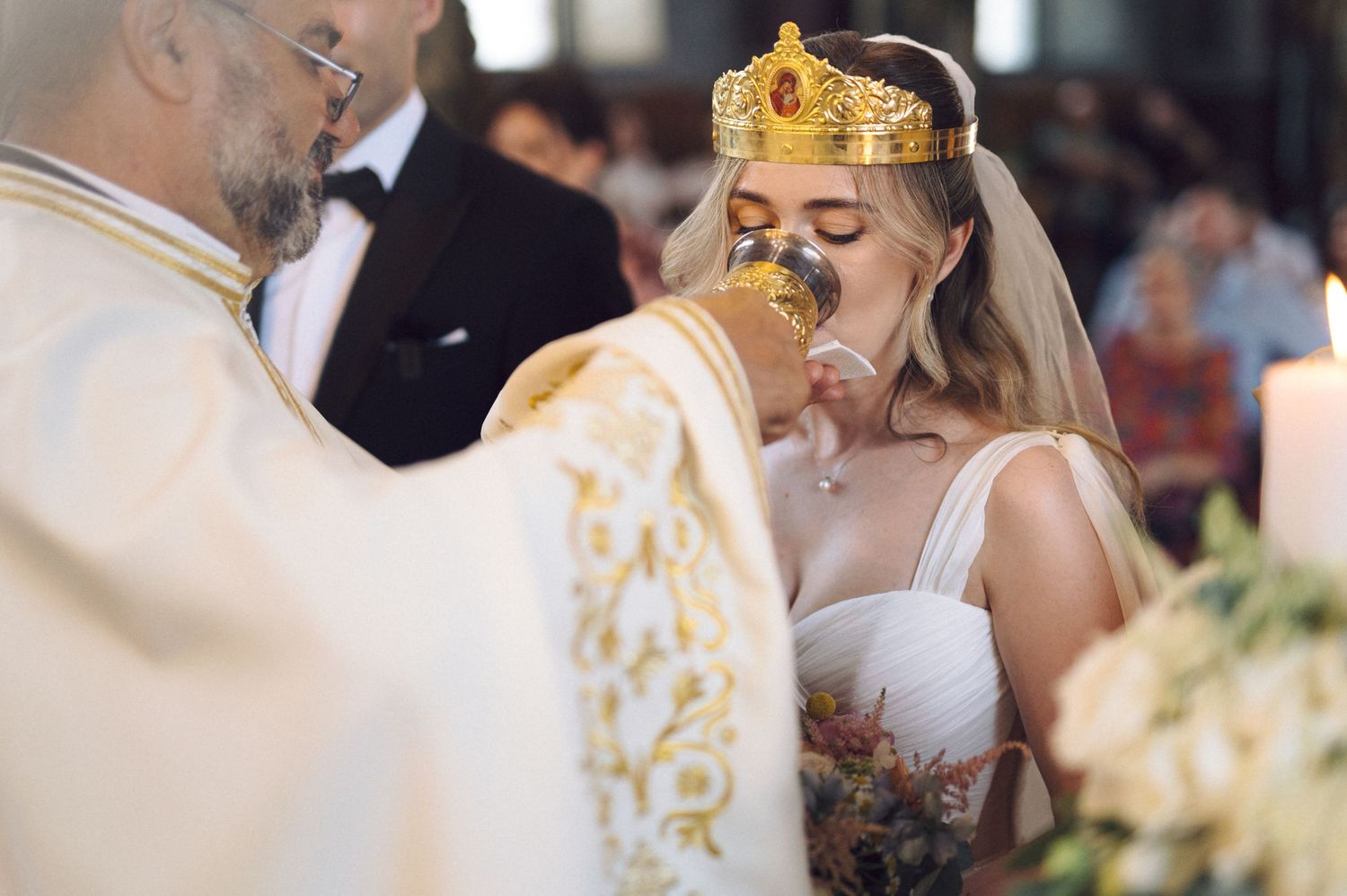 Orthodox Christian wedding ceremony with couple wearing traditional golden crowns during marriage ritual blessing.
