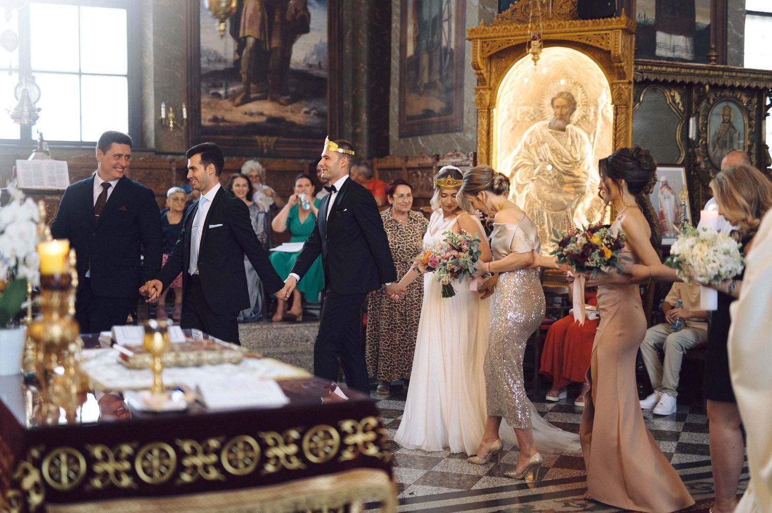 A wedding ceremony takes place inside an ornate church with guests and attendants gathered at the altar.