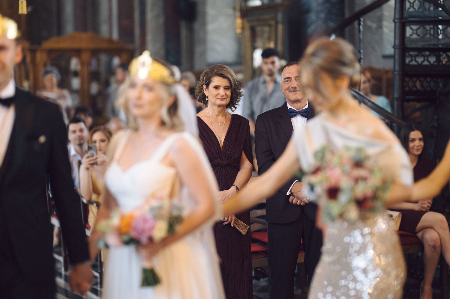 Wedding celebration scene in a church with guests watching the bridal party in formal attire and floral arrangements.