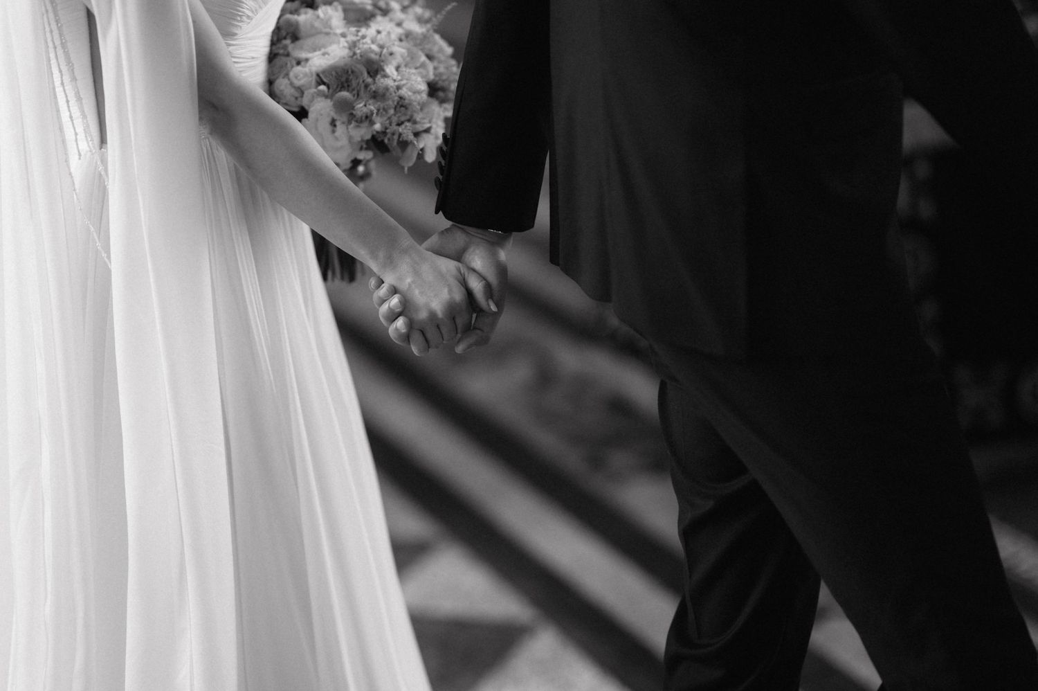 A stylish couple holds hands during their black and white wedding ceremony while guests look on in the background.