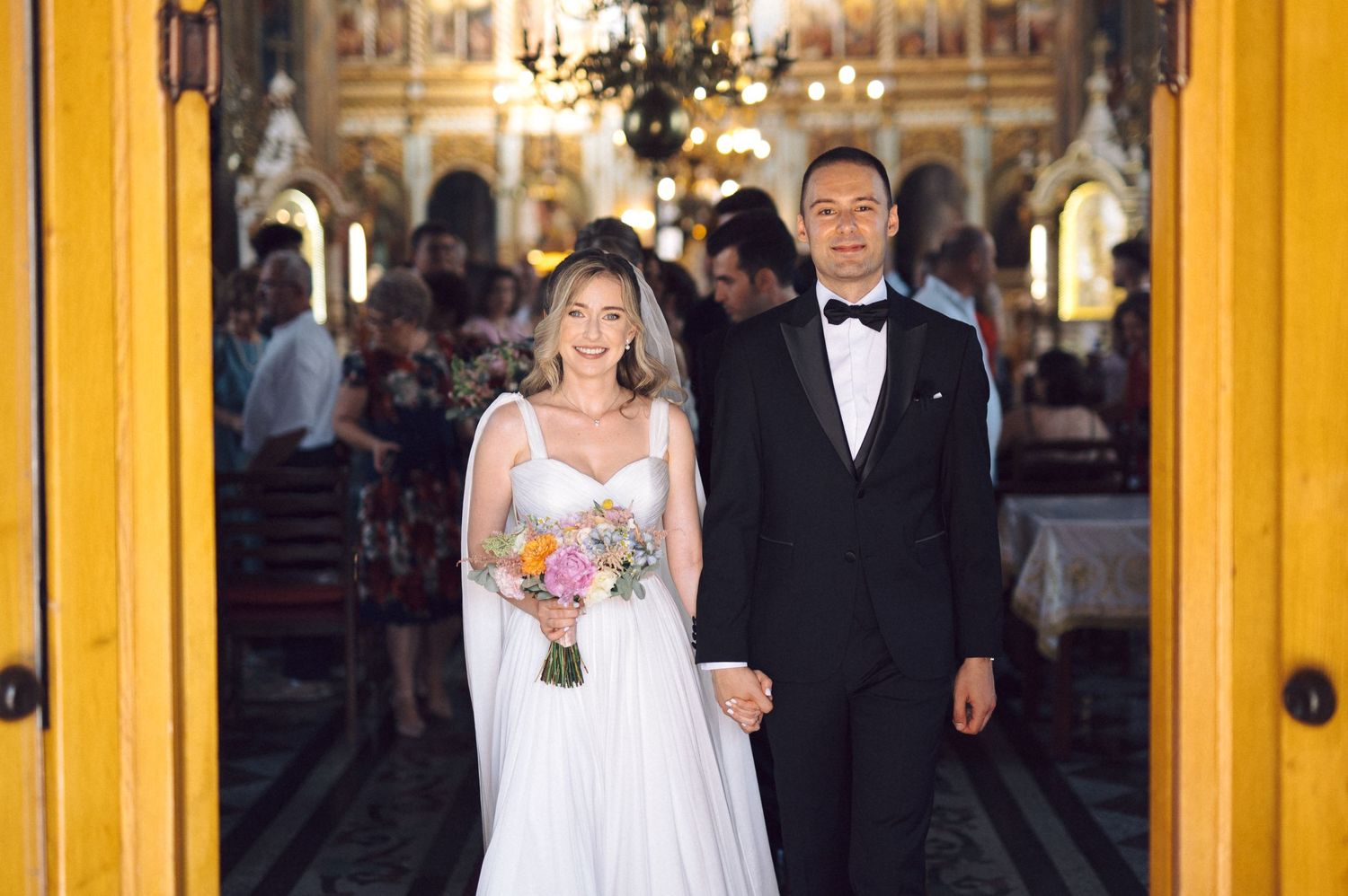 A couple at their wedding ceremony standing in church doorway with bride holding floral bouquet and groom in tuxedo.