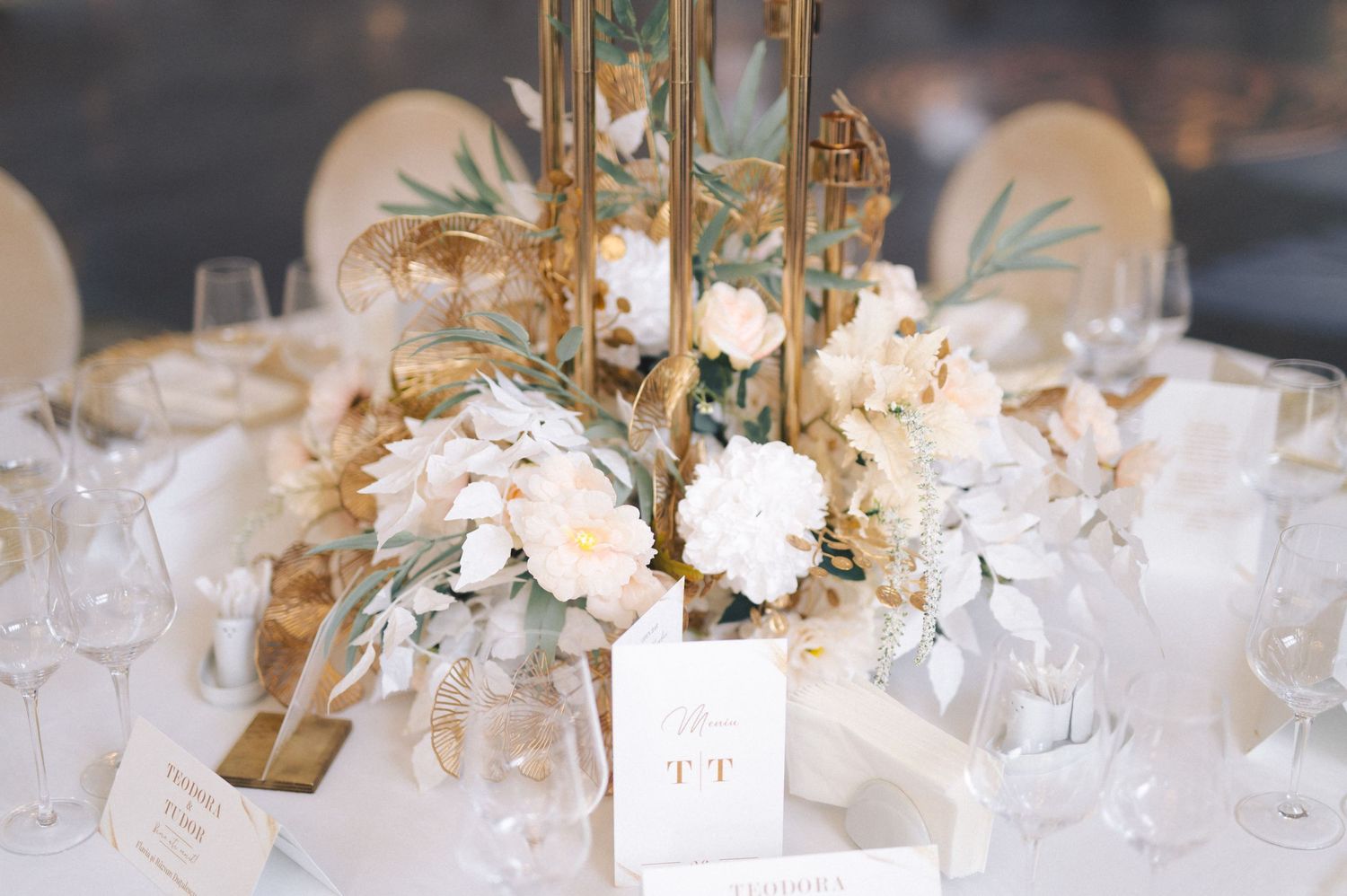 Elegant wedding centerpiece featuring white flowers, gold accents and dusty blue eucalyptus on a formal table setting.