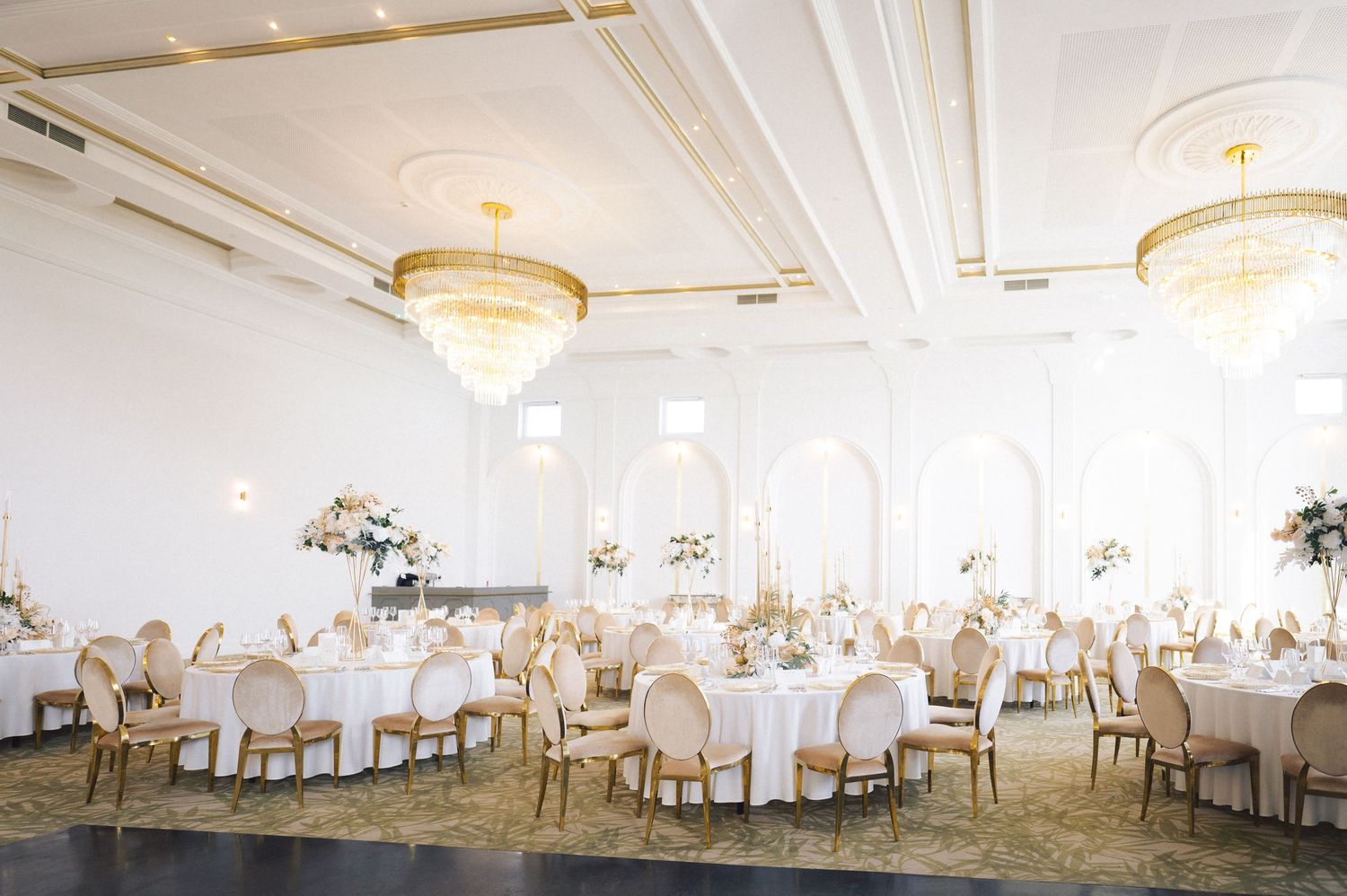 Elegant wedding reception ballroom with white tablecloths and decorative chandeliers illuminating the grand space.